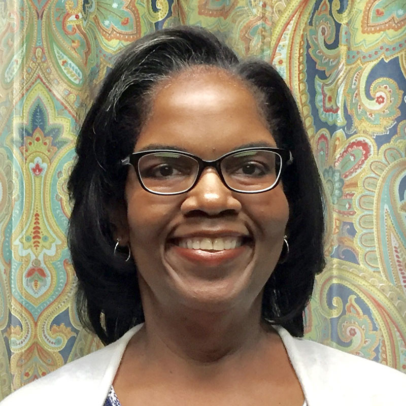 Dr. Wanda Addison poses in front of paisley wallpaper