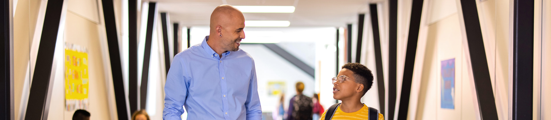 a bald man in a dress shirt walks and talks with an elementary school student