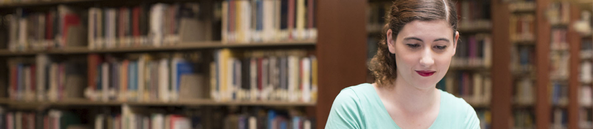 Woman with curly hair tied back in a aqua t-shirt sitting in Library