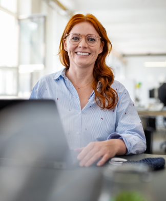 woman smiling happily at camera as her hands rest on laptop